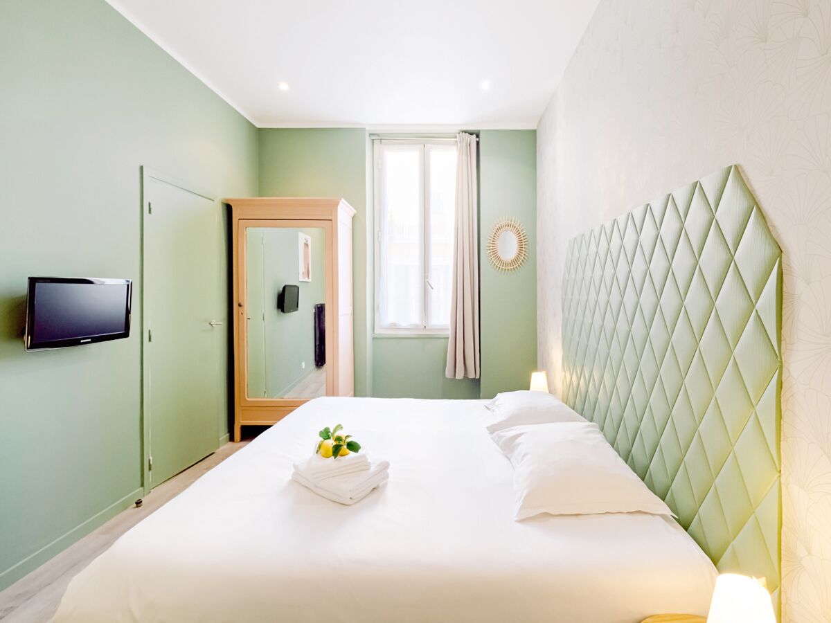Una cama bien hecha con una almohada y una toalla doblada, un televisor en la pared y un armario.