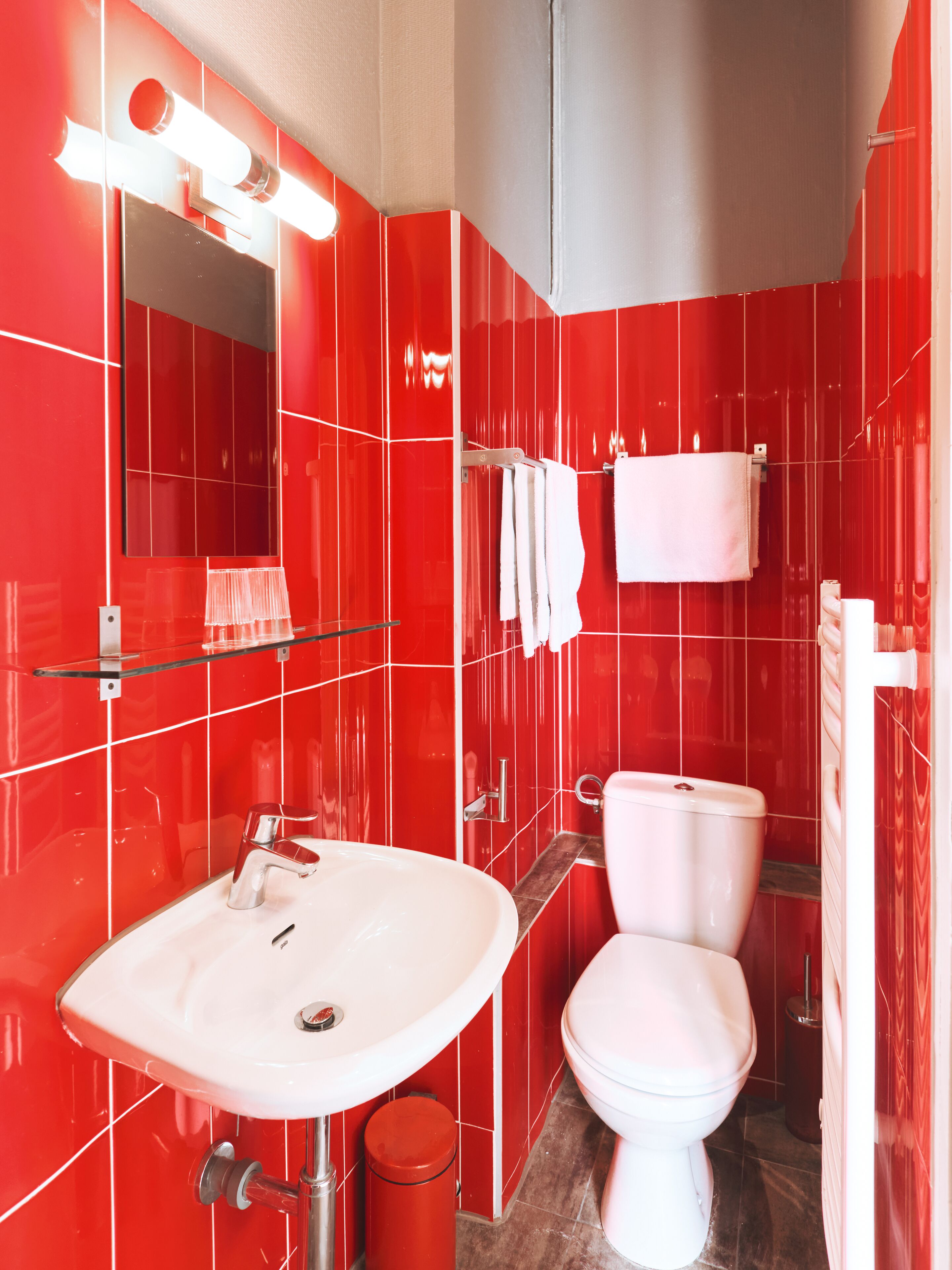 A modern bathroom with red tiles, a white sink, a toilet, and a glass shelf.