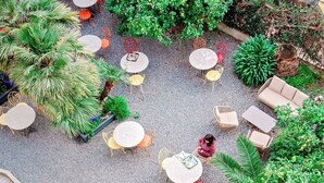 An outdoor seating area with round tables and chairs, surrounded by lush greenery and plants. - Hôtel Lemon (Menton)