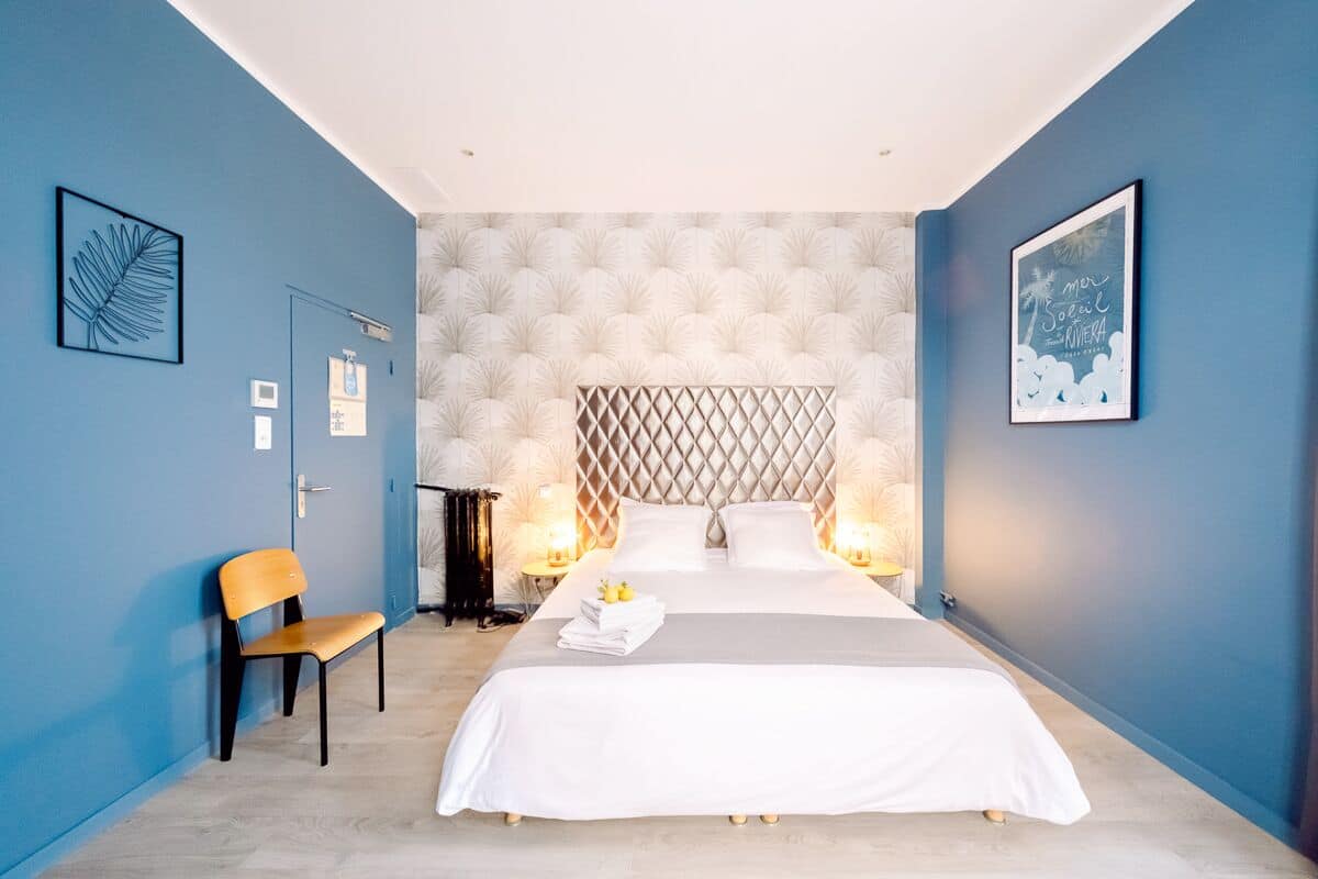A modern bedroom with a large bed, two bedside lamps, a chair, and artwork on the walls.