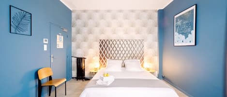 Een moderne slaapkamer met een groot bed, twee bedlampjes, een stoel en kunstwerken aan de wanden.