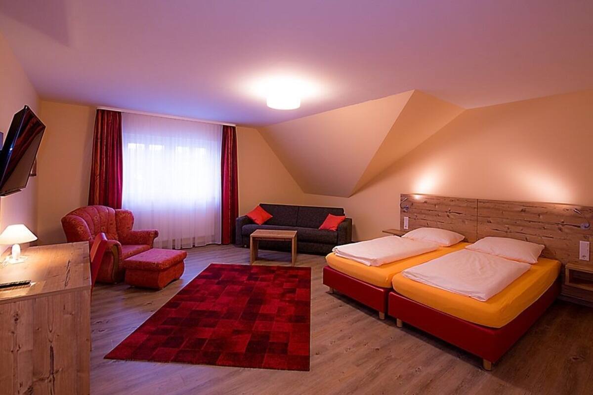 Quarto com duas camas, um sofá, uma cadeira, uma mesinha e uma televisão.