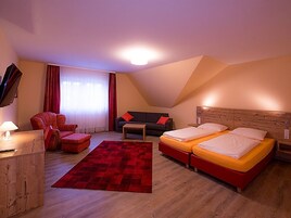 Quarto com duas camas, um sofá, uma cadeira, uma mesinha e uma televisão.