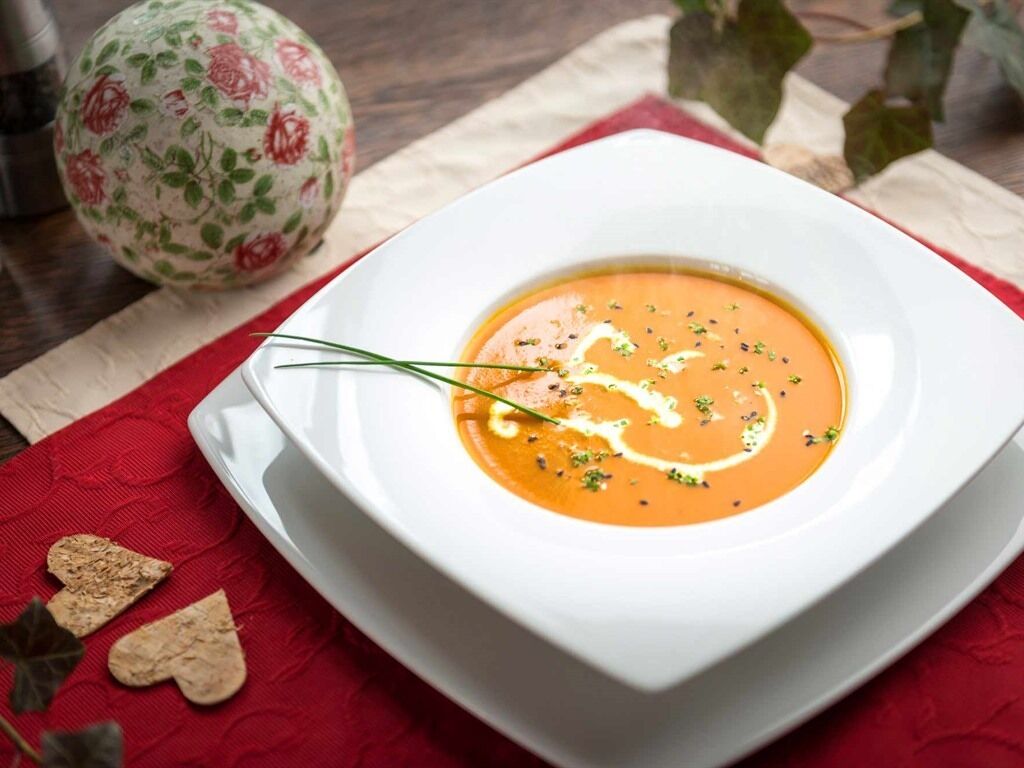 A bowl of soup on a white plate with a red napkin underneath.
