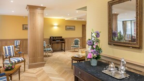 A hotel room with a wooden floor, a large mirror, a dining table with chairs, and a flower arrangement on the side table. - Home Médicis Les Petites Roches (Dijon)