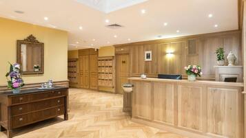 A hotel lobby with a wooden reception desk, a large mirror, and a herringbone-patterned floor.