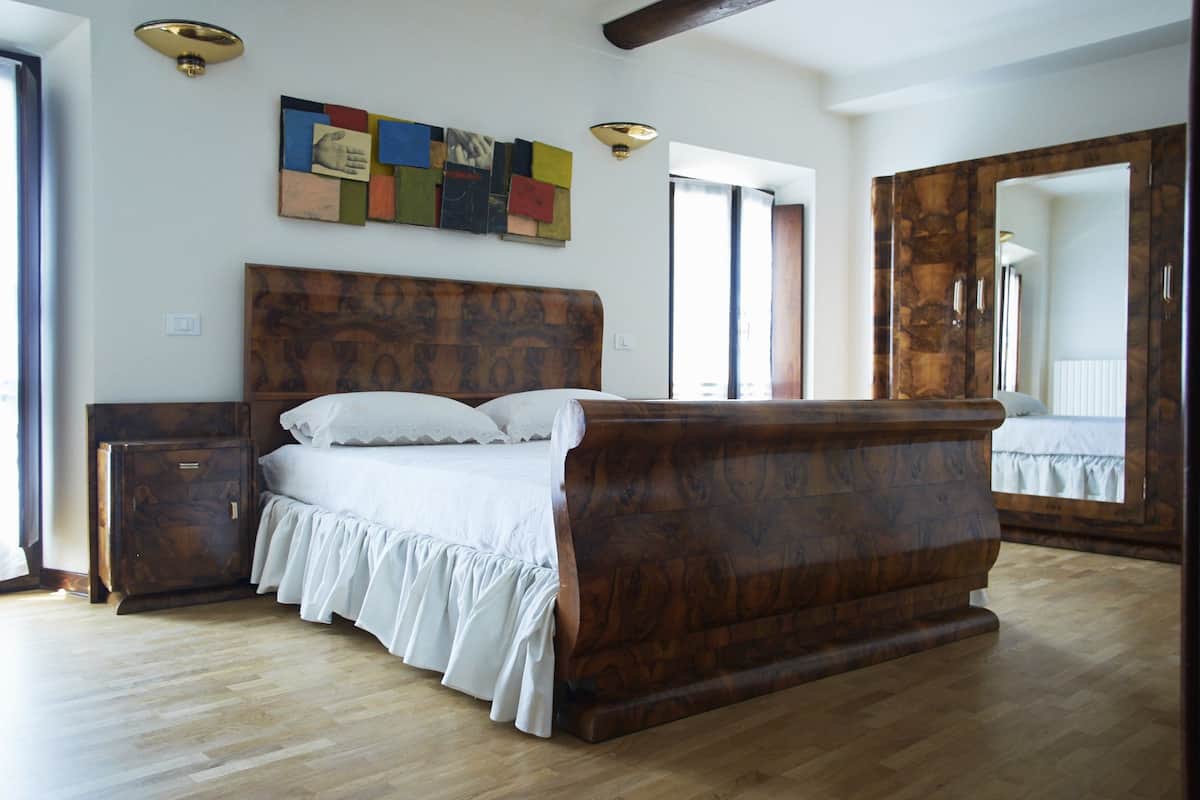 Une chambre à coucher avec un lit en bois, une table de chevet, une commode et un grand miroir.