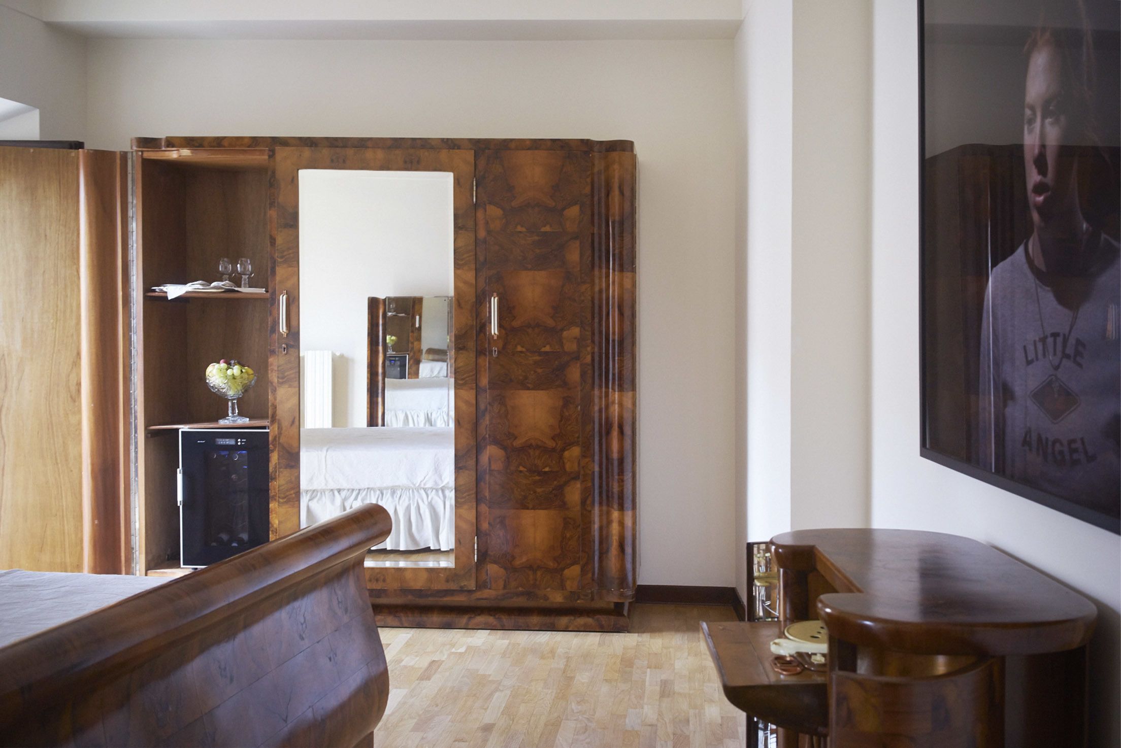 A bedroom with a wooden wardrobe, a bed, a small bedside table, and a mirror.