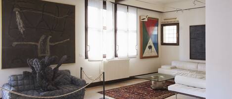 A modern living room with a large abstract painting, a white sofa, and a unique seating area.