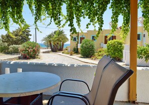 A balcony with a table and chairs, overlooking a street with buildings and a view of the sea. - Grandes Apartments Kouremenos (Sitia)