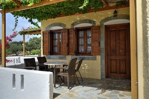 A covered outdoor seating area with wicker chairs and a table, stone flooring, and a pergola with climbing plants.