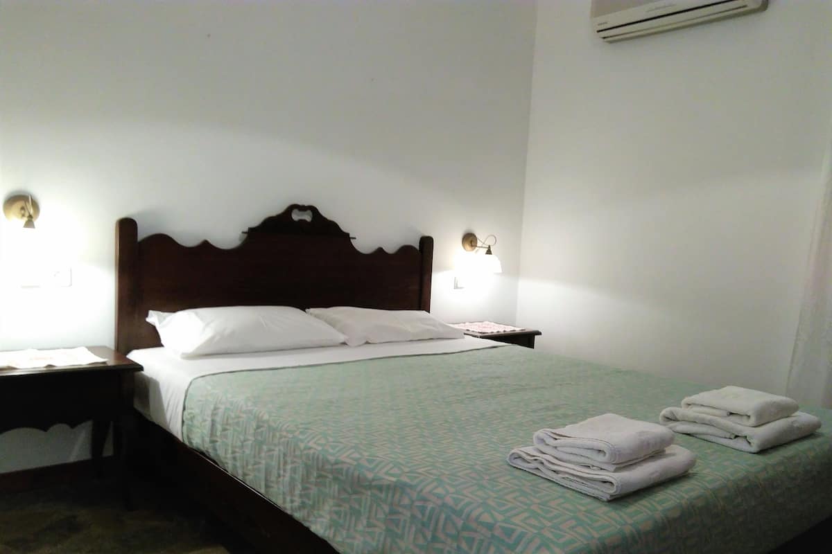 A hotel room with a bed, two bedside tables, a wall-mounted air conditioner, and a patterned bedspread.