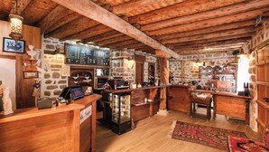 Un interior rústico de madera con pared de piedra, vigas de madera en el techo, una zona de bar y una recepción.