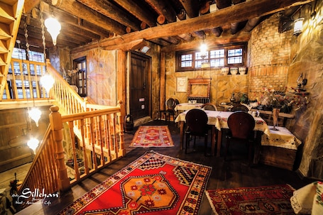 A rustic interior with wooden beams, a staircase, and a dining area with tables and chairs.