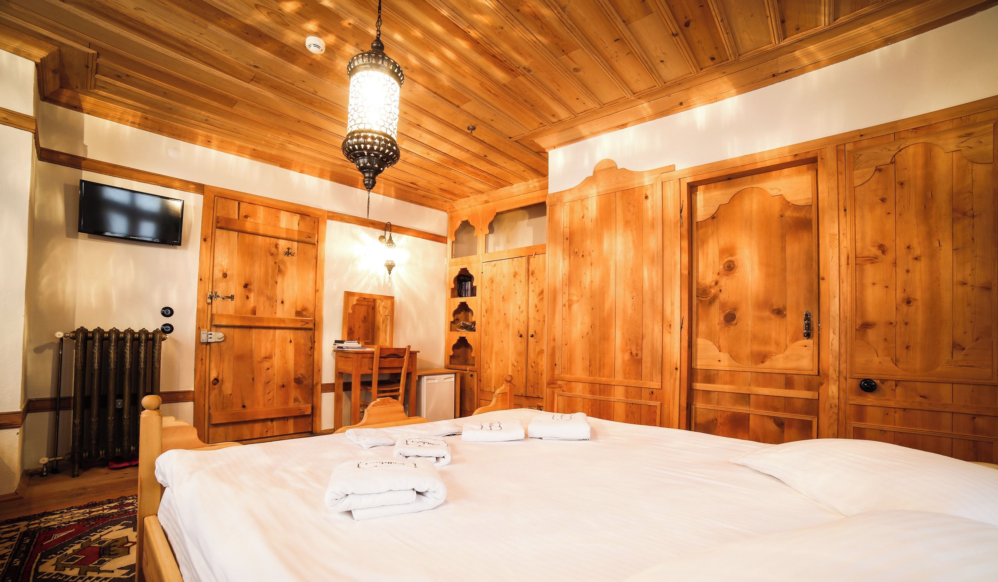 A wooden room with a bed, a television, and a desk.