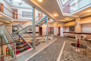 Un hall amplio con una escalera central, varias zonas de descanso y un jarrón decorativo sobre una mesa redonda.