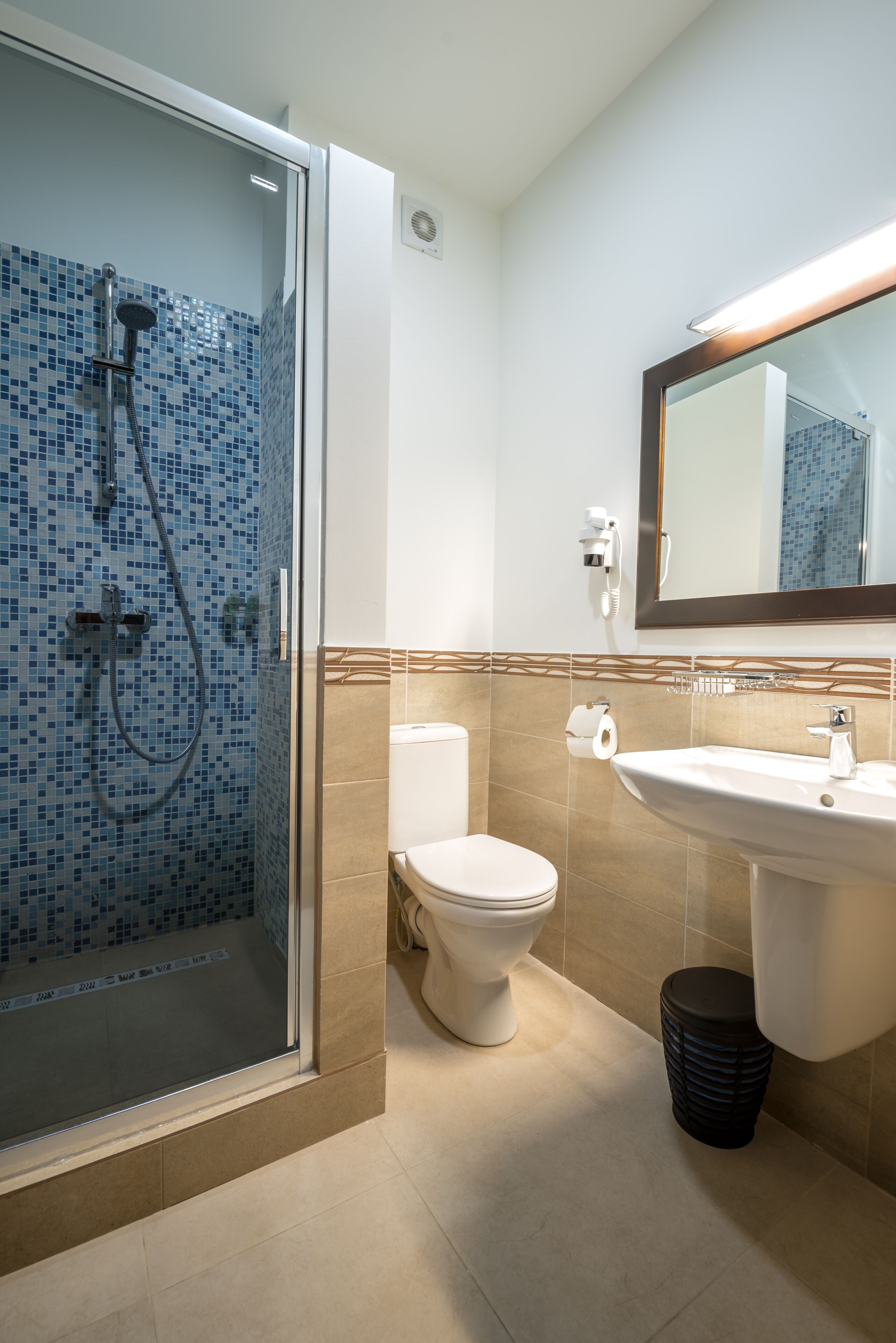 A bathroom with a glass-enclosed shower, a toilet, and a sink with a mirror above it.