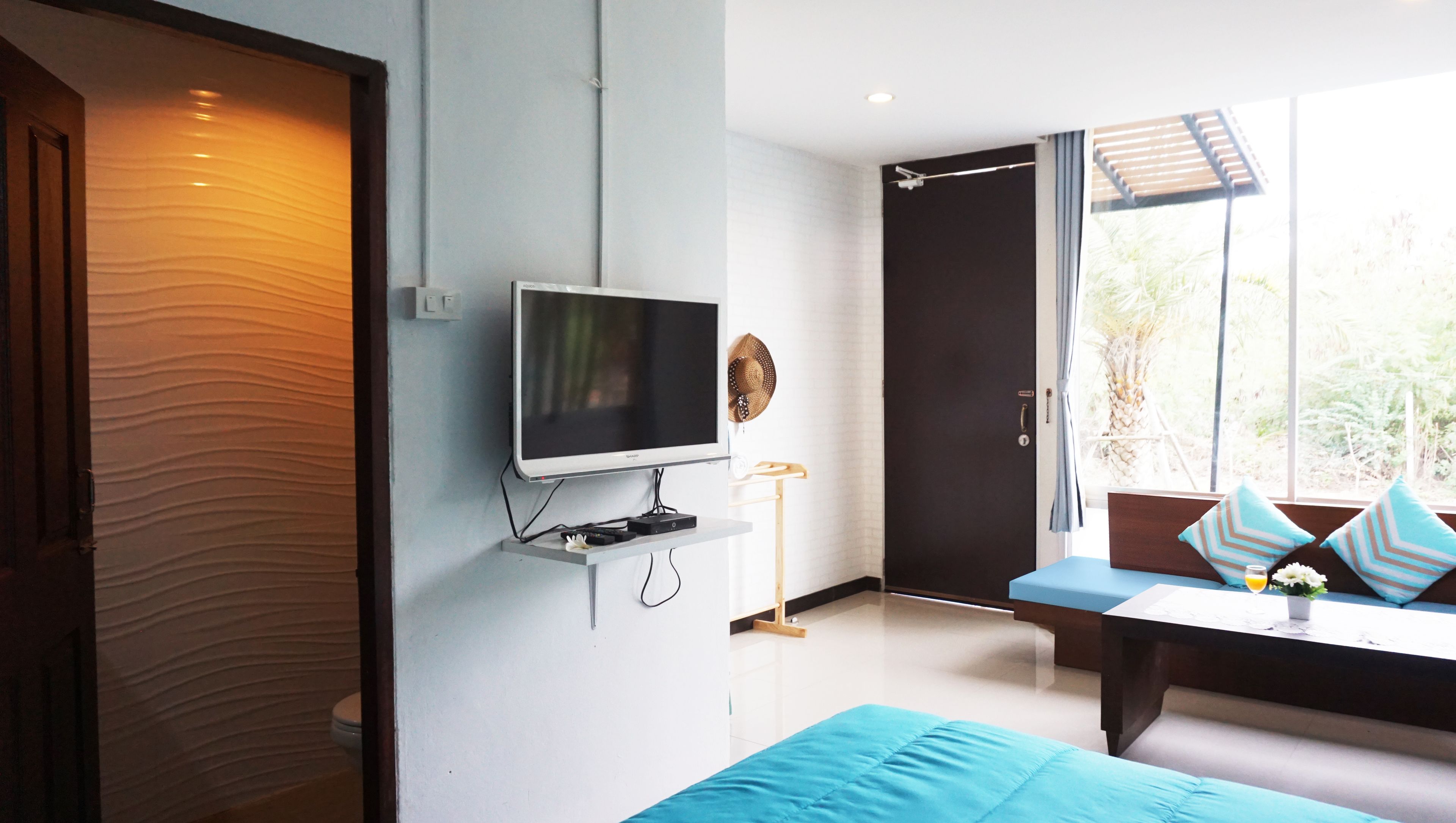 A modern room with a flat-screen TV mounted on the wall, a sofa with blue cushions, and a large window offering a view of greenery outside.
