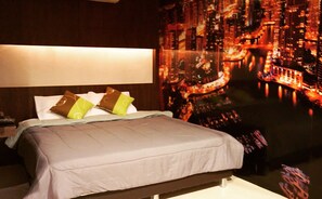 A hotel room with a bed, pillows, a nightstand, and a large cityscape tapestry on the wall. - Me'vela Boutique Resort (Cha-am)