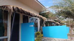 Una casa con techo de paja, un portón azul y una palmera en el jardín.