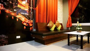 Una sala moderna con un sofá marrón oscuro, cortinas naranja y una pequeña mesa con un jarrón de flores.