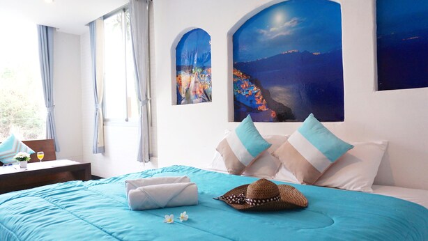 Una habitación de hotel con una cama, almohadas, un sombrero y una ventana con cortinas.