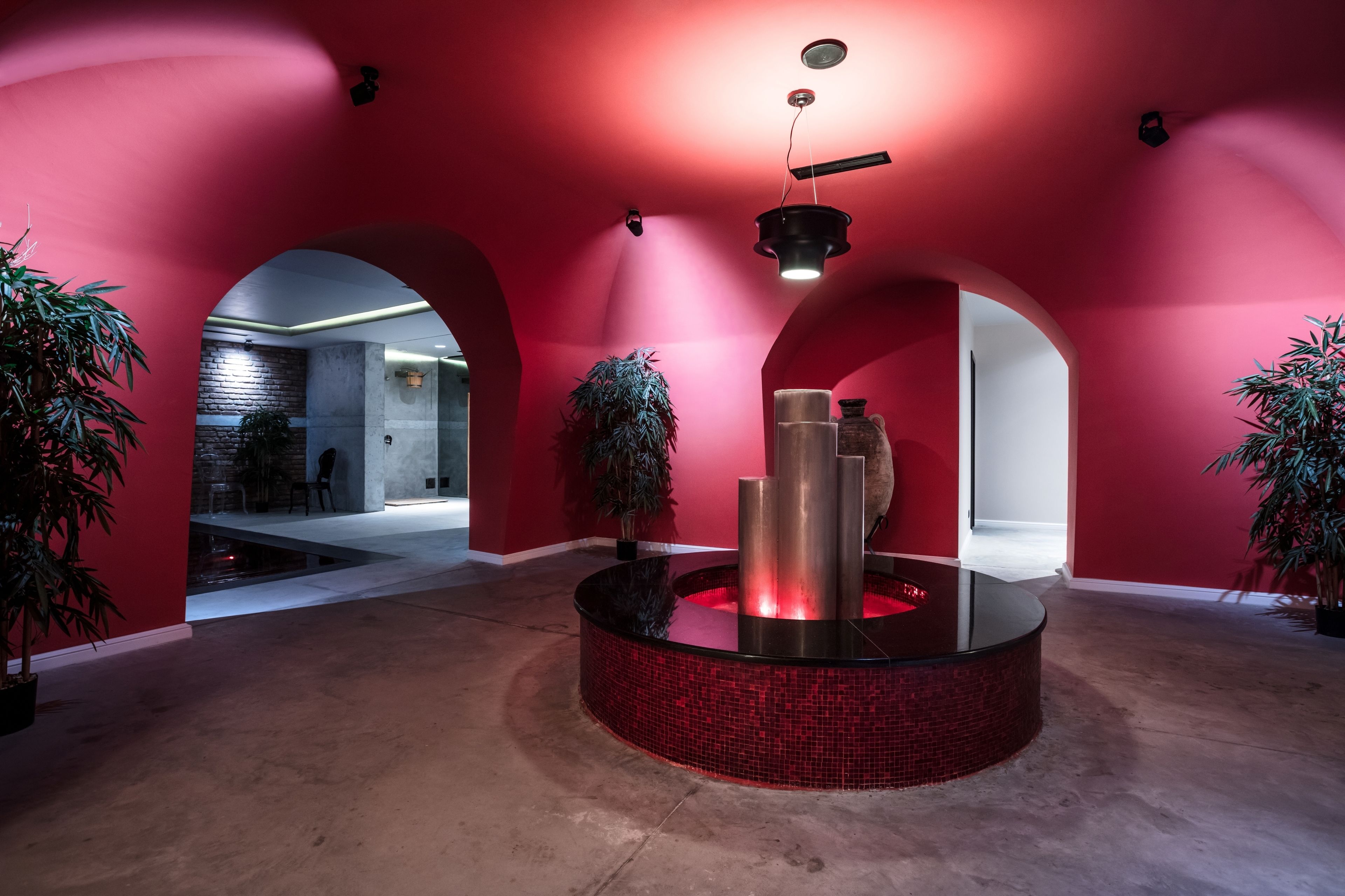Un intérieur moderne avec des murs rouges, un élément central circulaire doté d’une structure métallique et des plantes en pot.