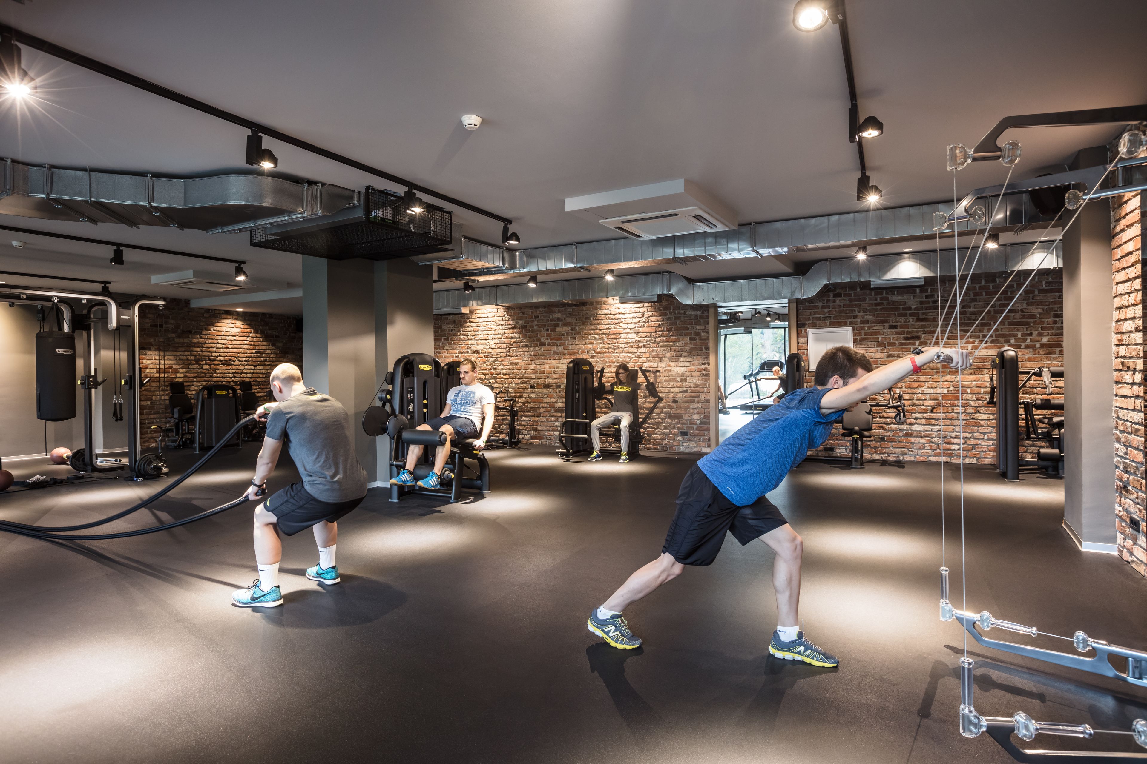 Una palestra con attrezzature per esercizi, un muro in mattoni e una persona che utilizza un elastico di resistenza.
