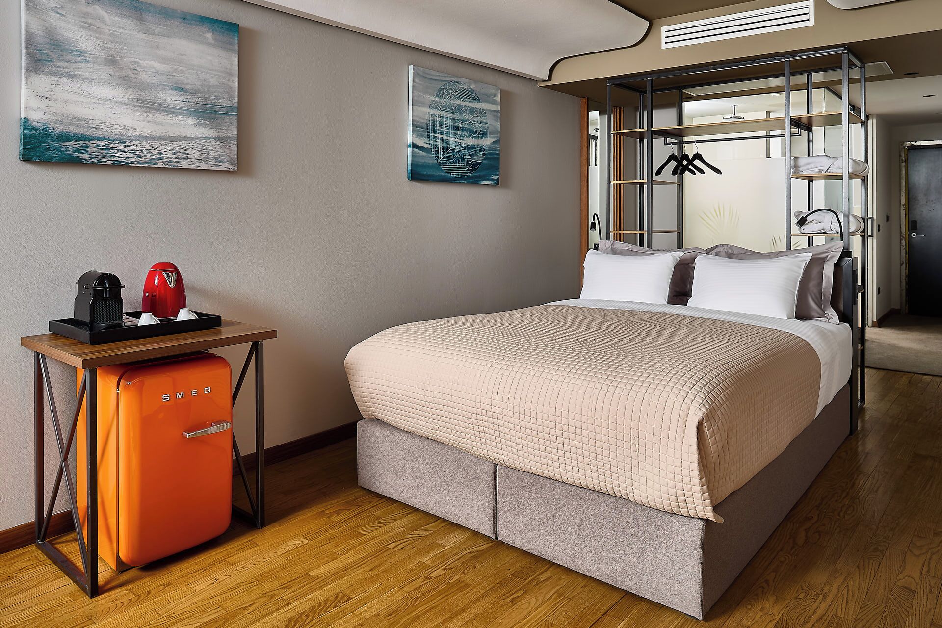 A modern hotel room with a bed, a compact kitchenette, and artwork on the walls.