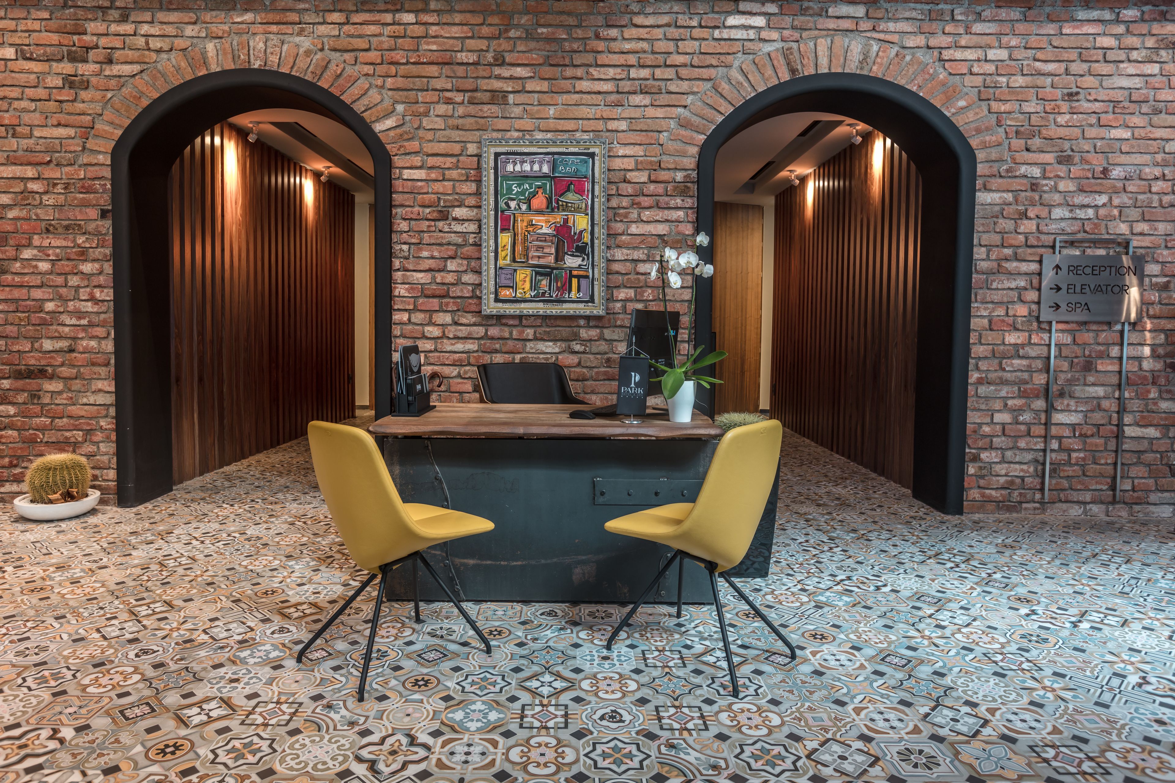 Een receptiegedeelte met een bakstenen muur, twee houten deuren, een receptiebalie en een vloer met een patroon.
