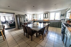 A modern kitchen with a central island, dark wooden chairs, and a large dining table.