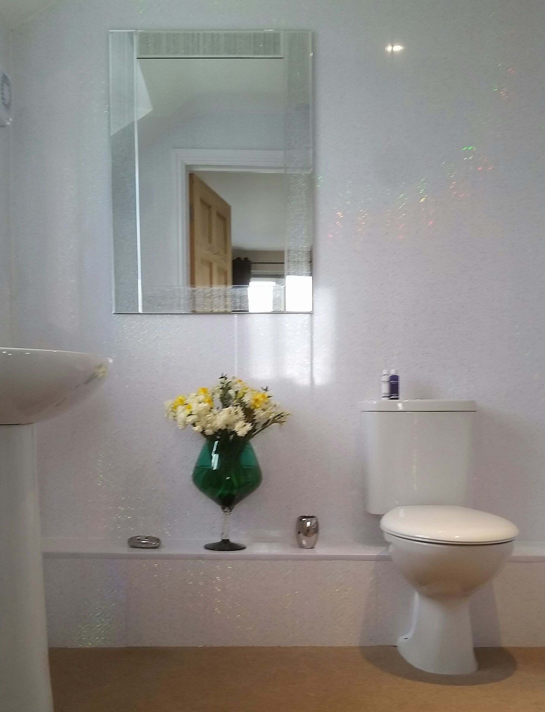 A bathroom with a toilet, a sink, a mirror, and a vase with flowers.