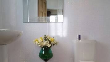 A bathroom with a toilet, a sink, a mirror, and a vase with flowers.