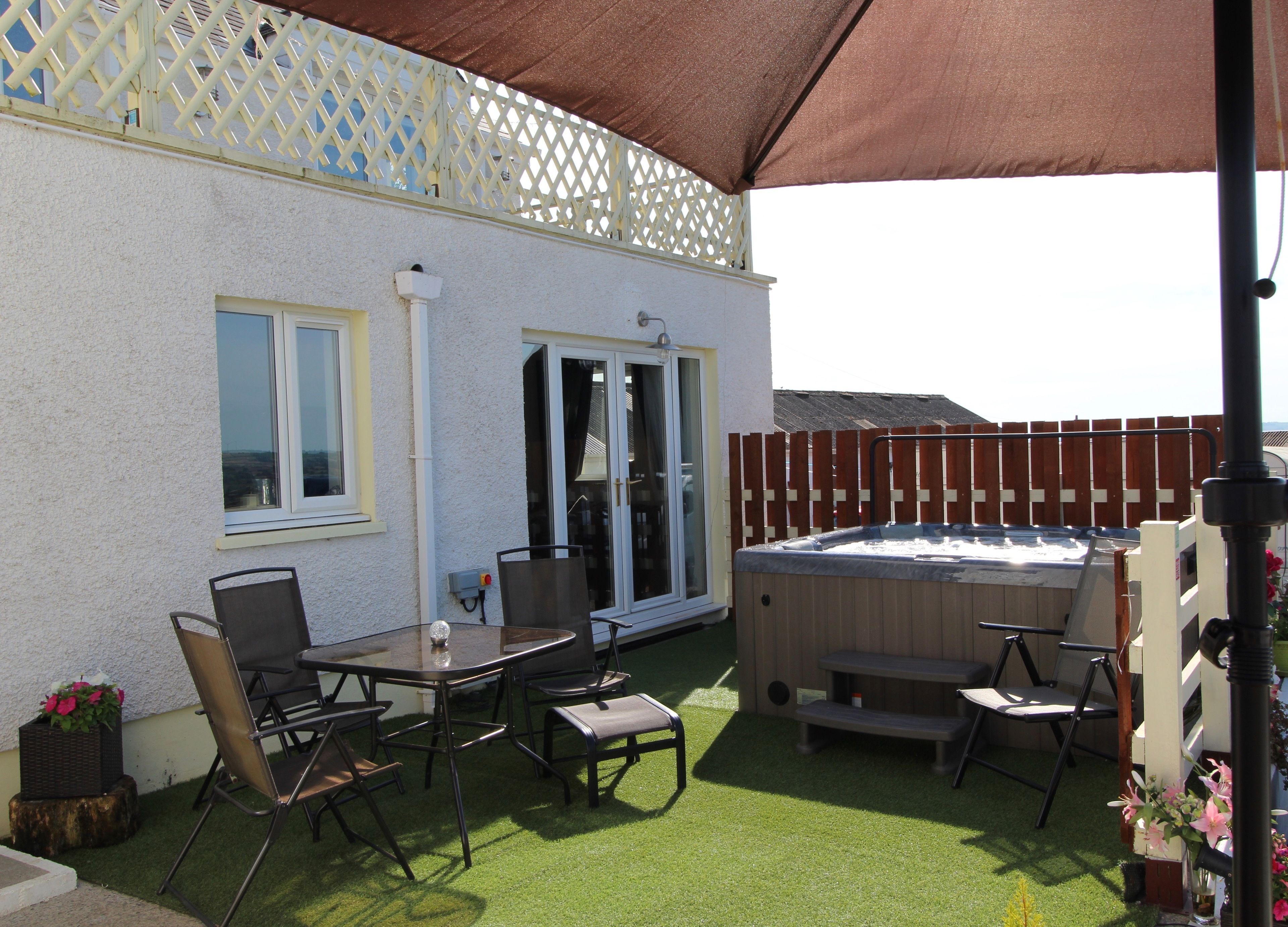 A patio with a hot tub, outdoor seating, and a white building with a lattice window.