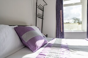 A bed with a white and purple bedspread, a purple pillow, and a black metal headboard. - Pantysgyfarnog (Carmarthen)