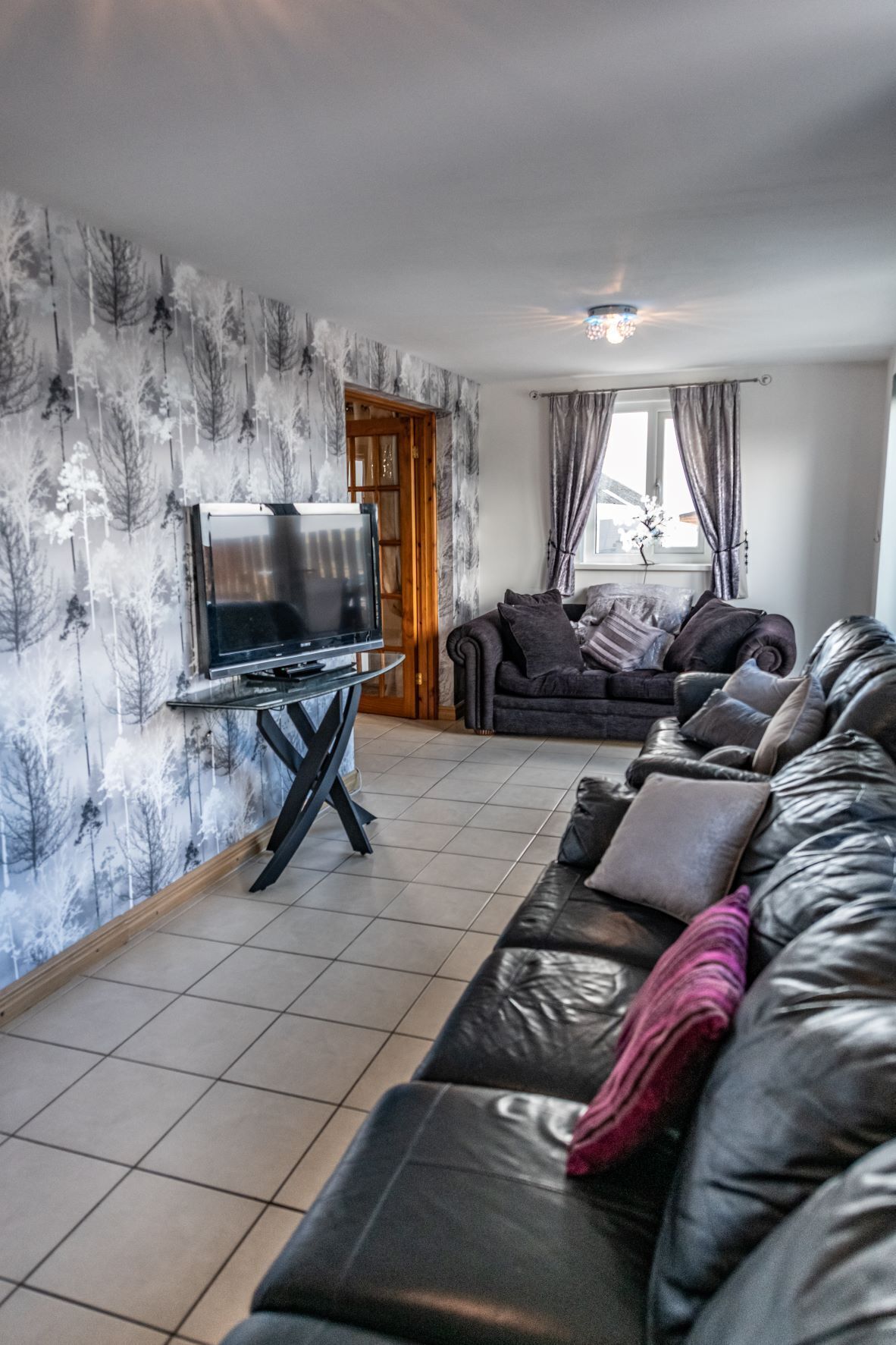 A living room with a sofa, a TV, and a patterned wallpaper.