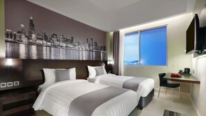Habitación de hotel con dos camas, un mural con vistas a la ciudad, un escritorio con silla y un amplio ventanal.