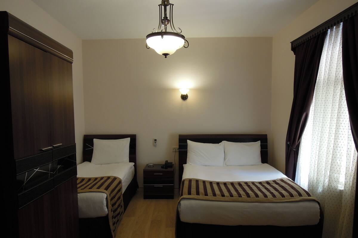 Une chambre d’hôtel avec deux lits simples, une armoire, une table de chevet et un luminaire au plafond.