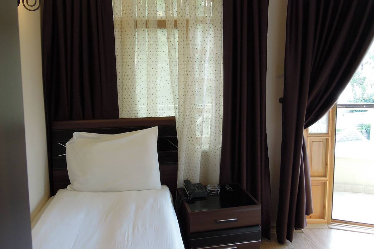 Une chambre d’hôtel avec un lit, une table de chevet avec un téléphone, une lampe et une fenêtre avec des rideaux.