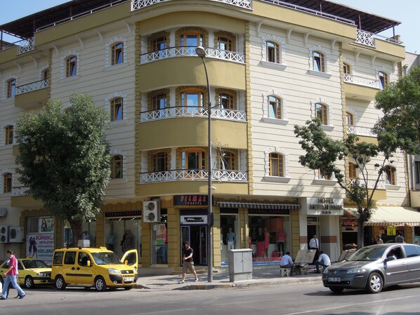 Un hotel de varios pisos con balcones, una tienda en la planta baja y un coche estacionado.