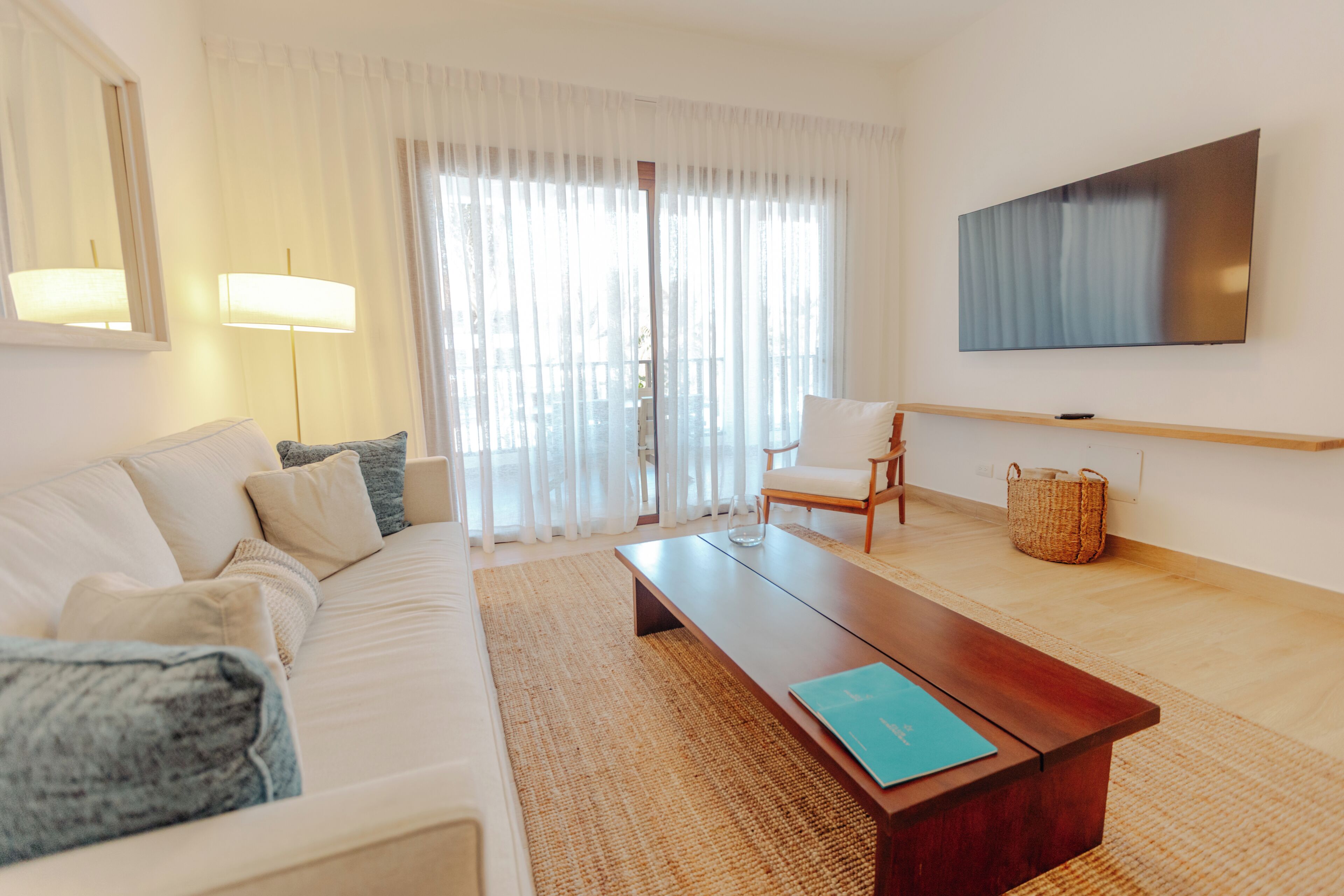 A modern living room with a sofa, a coffee table, a TV, and a large window with curtains.