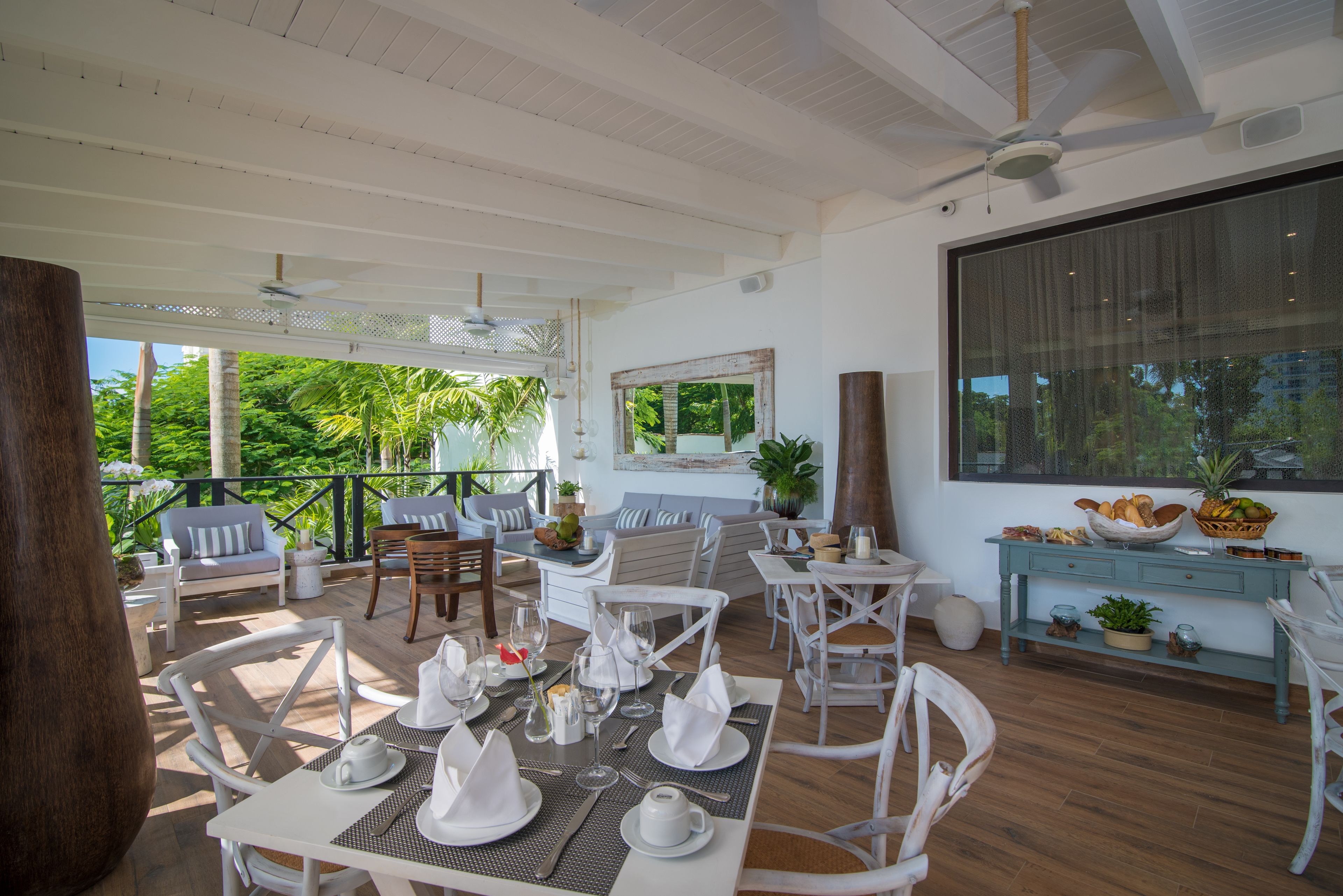 A spacious outdoor dining area with white furniture, a large window, and a view of greenery.