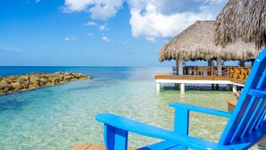A clear blue sea, a thatched-roof structure, and a wooden deck with chairs. - Hotel Casa Hemingway (Guayacanes)
