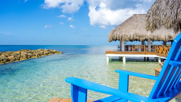 A clear blue sea, a thatched-roof structure, and a wooden deck with chairs. - Hotel Casa Hemingway (Guayacanes)