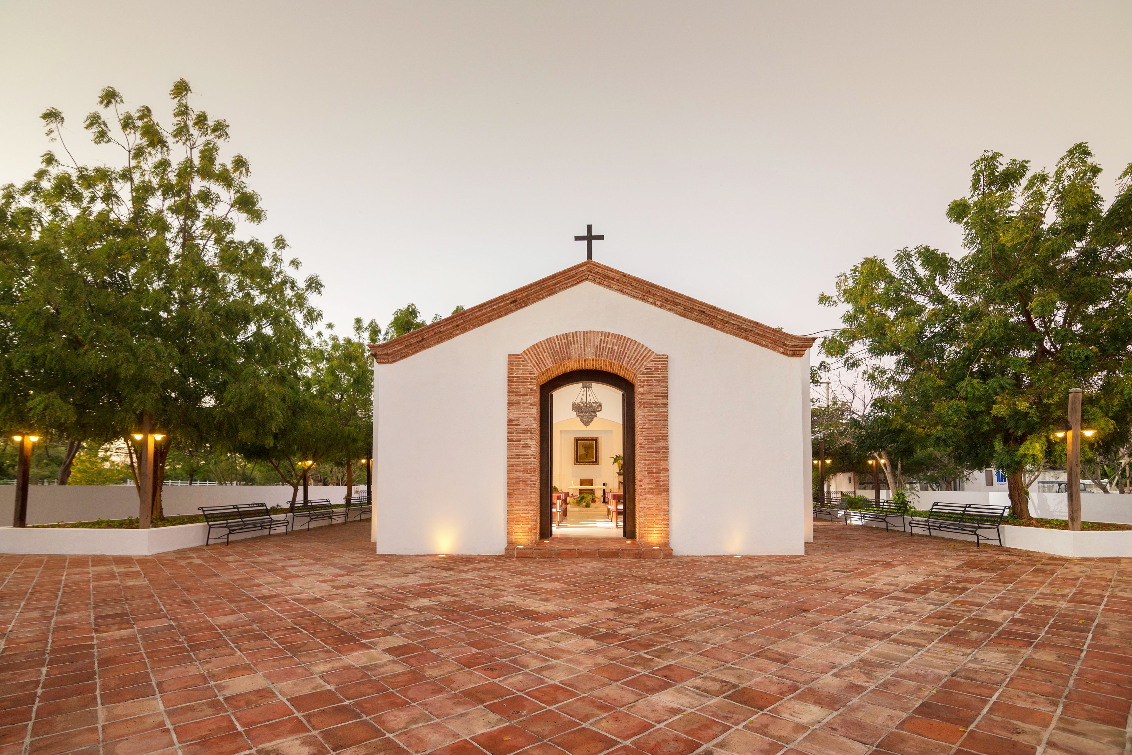 Uma pequena igreja com uma cruz no topo, um arco de tijolos e piso de azulejos.
