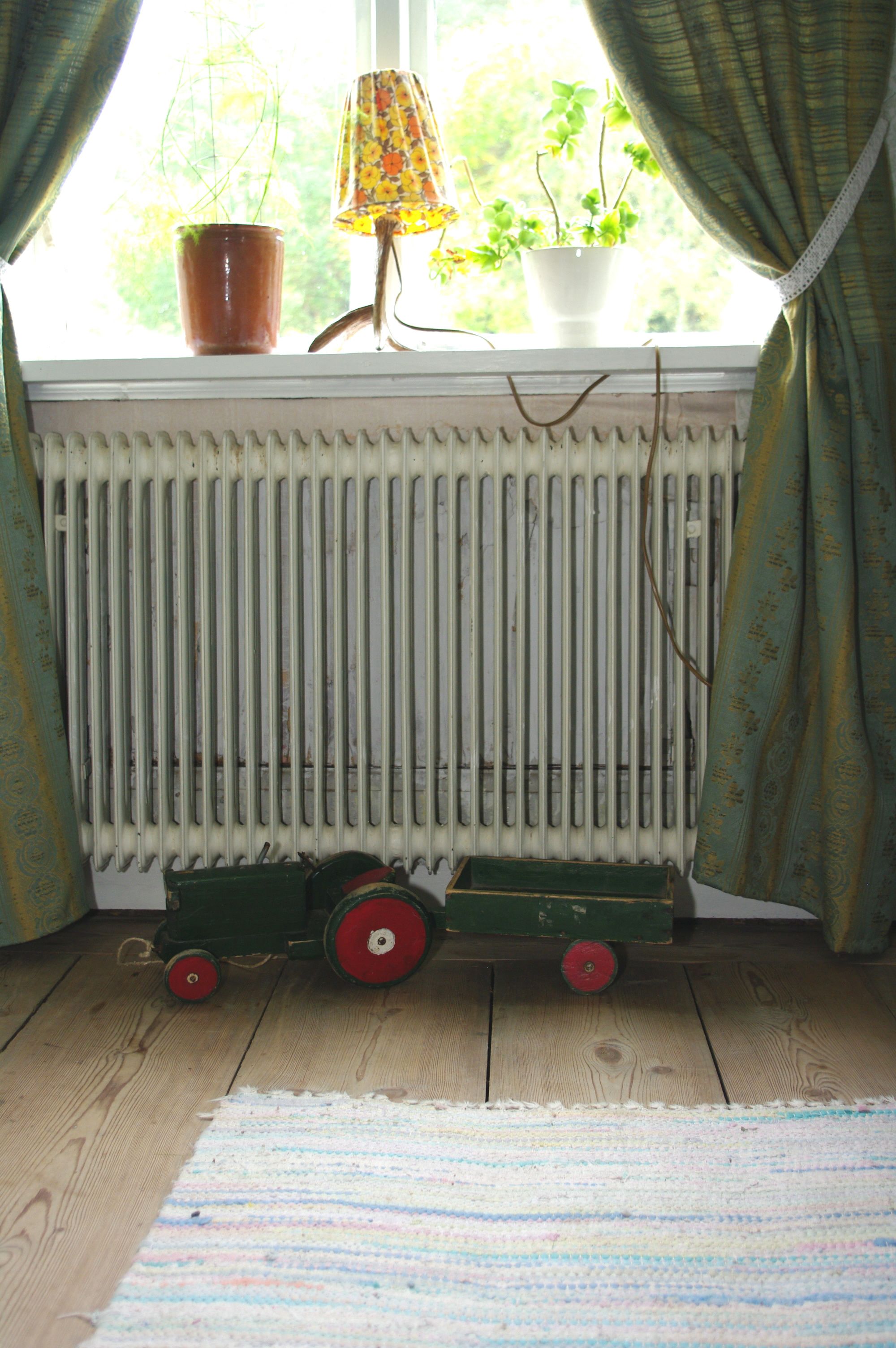 A radiator, a window with curtains, a potted plant, and a toy train on a windowsill.