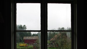 A window with a view of a rural landscape, including a barn and a small house.