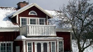 A two-story wooden house with a balcony, surrounded by snow.