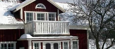 A two-story wooden house with a balcony, surrounded by snow.