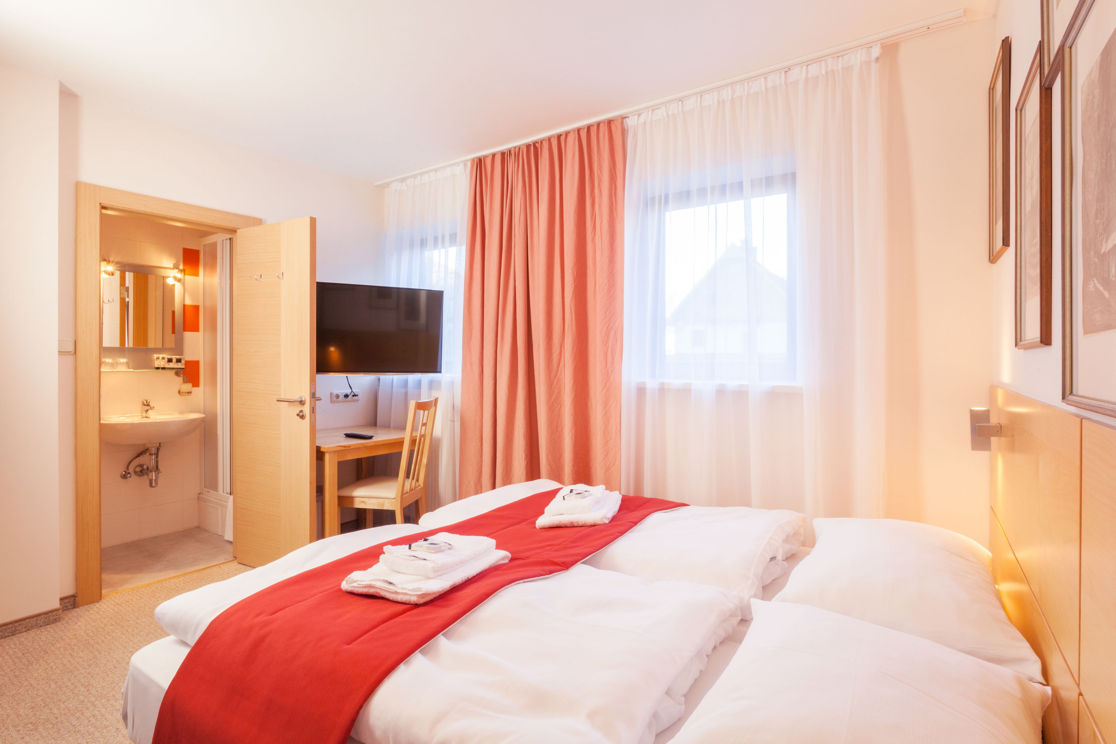 Ett hotellrum med en säng, ett skrivbord, en stol, en tv och ett badrum.